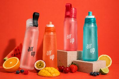 Four Air Up reusable water bottles in pastel colours arranged with fresh fruit on a coral background.